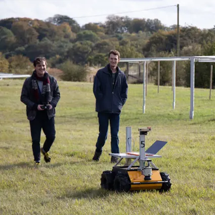 Two men walking with a robot in a solar farm.